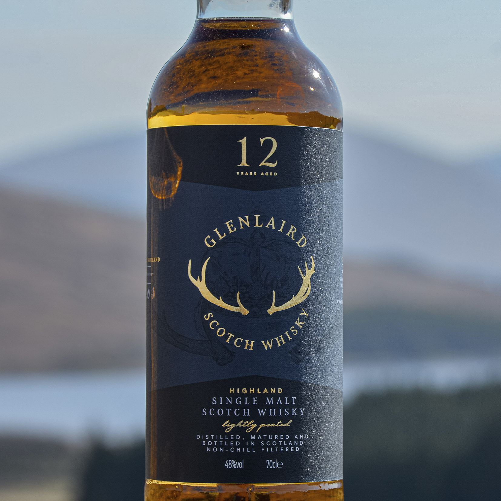 Highland spirit Product photo of Glenlaird whisky shot in the Highlands, featuring a bottle of the single-malt Scotch whisky set against a backdrop of rolling hills. The scenic landscape emphasizes the whisky's Scottish heritage. Photography by Studio Hart.